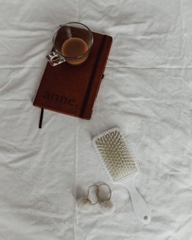 Flat lay of a notebook, coffee cup, hairbrush, and earrings on white fabric.