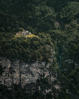 A serene view of houses atop a lush forested cliff with cascading waterfalls.