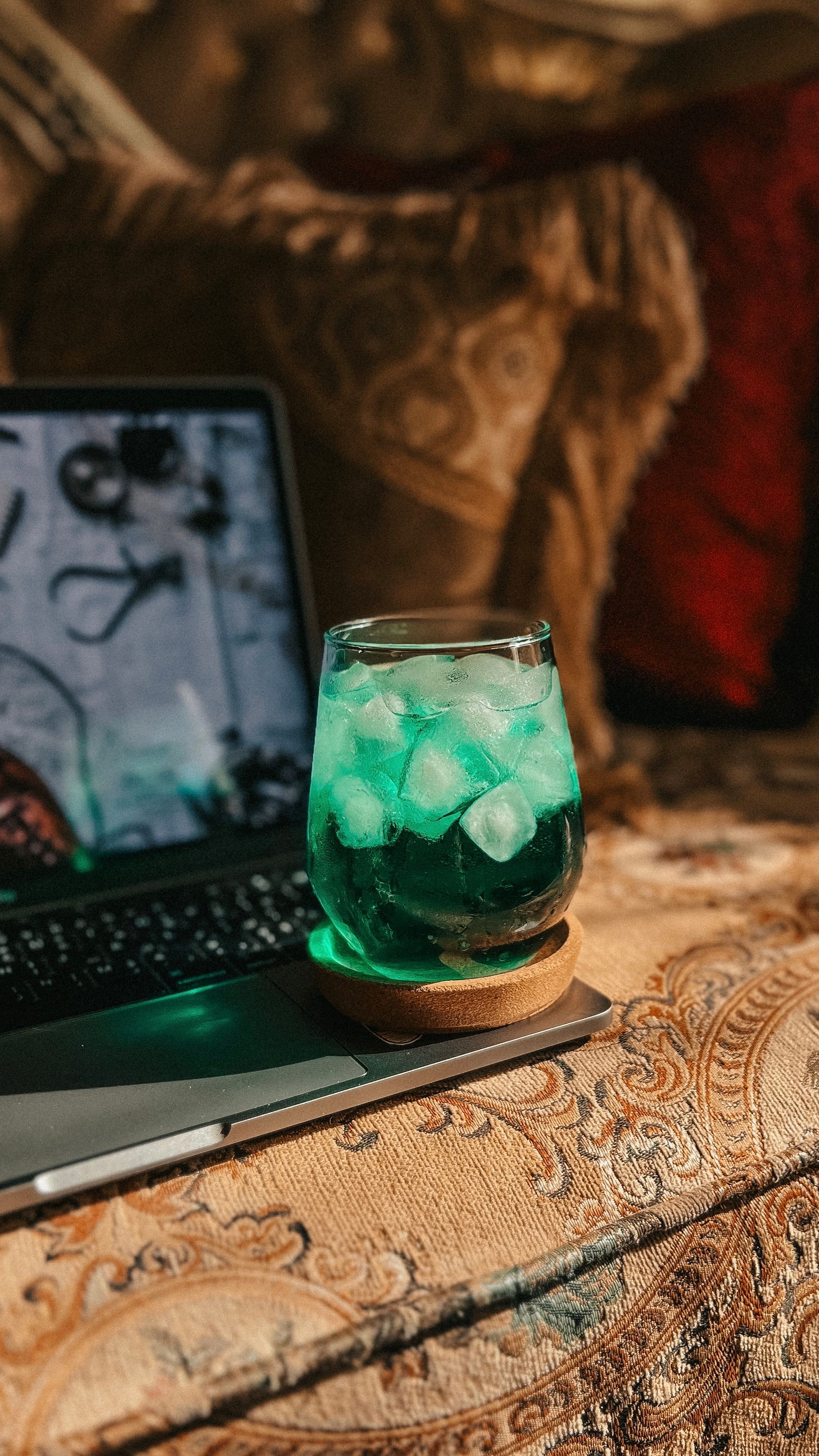 A refreshing green beverage with ice on a cozy couch next to a laptop in ambient lighting.