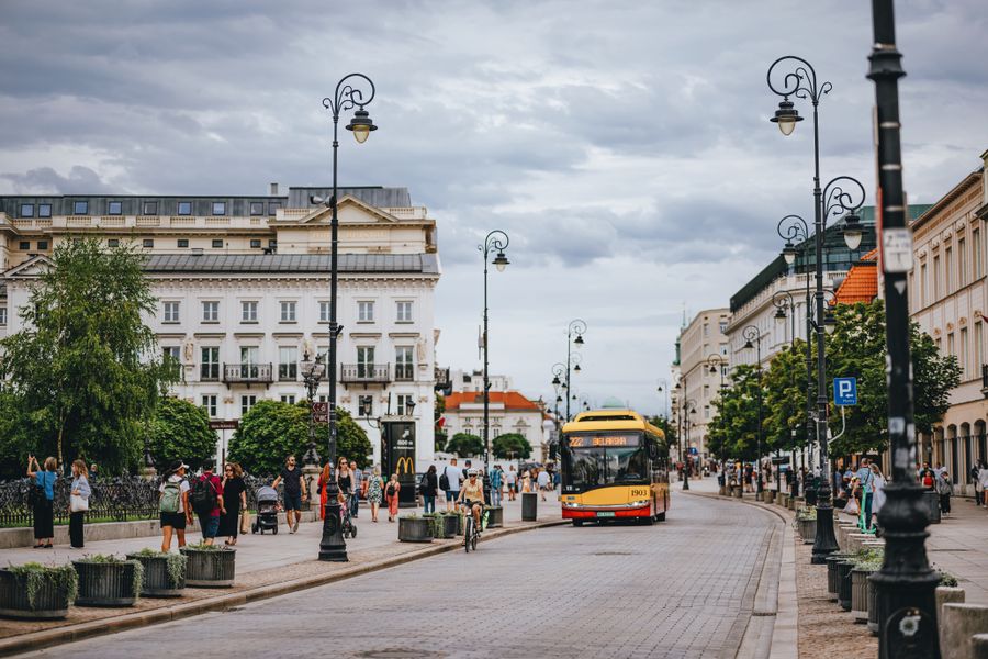 Bustling Warsaw street with modern bus and pedestrians, showcasing urban life.