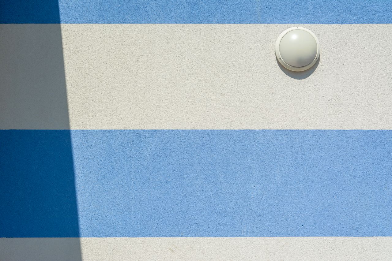 close up of a blue and white striped wall with a round wall lamp casti