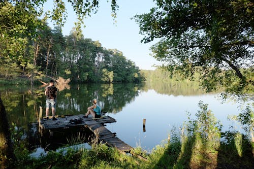 Two people are sitting on a dock near a lake