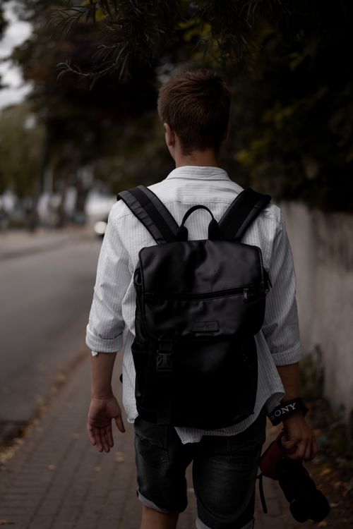 Free Casual stroll on city sidewalk with black backpack in focus. Stock Photo