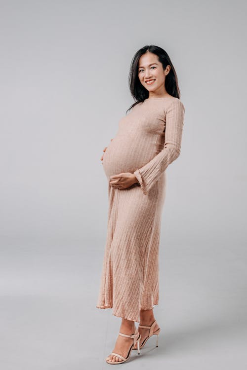 Pregnant Brunette Woman in Pink Maxi Dress Posing in a Studio