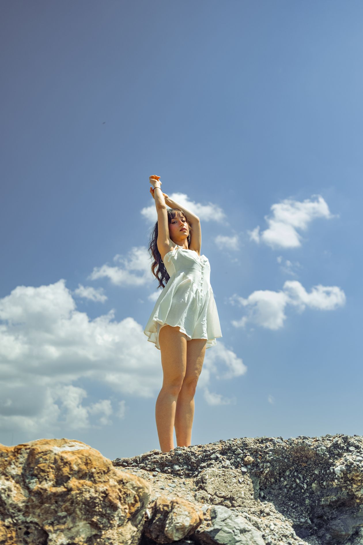 Woman in a short white dress standing on a rocky shore