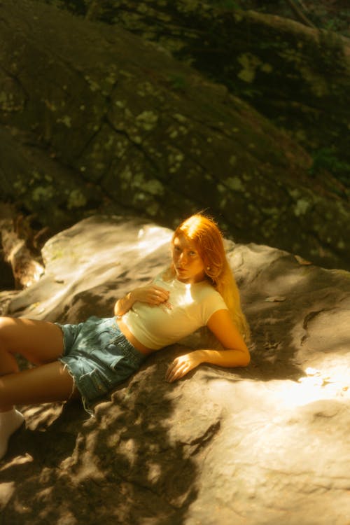 Model in a White Crop Top and Denim Shorts Lying on a Rock in the Forest