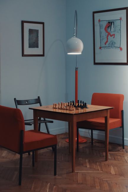 Modern interior with chess set on wooden table, orange chairs, and unique lamp.