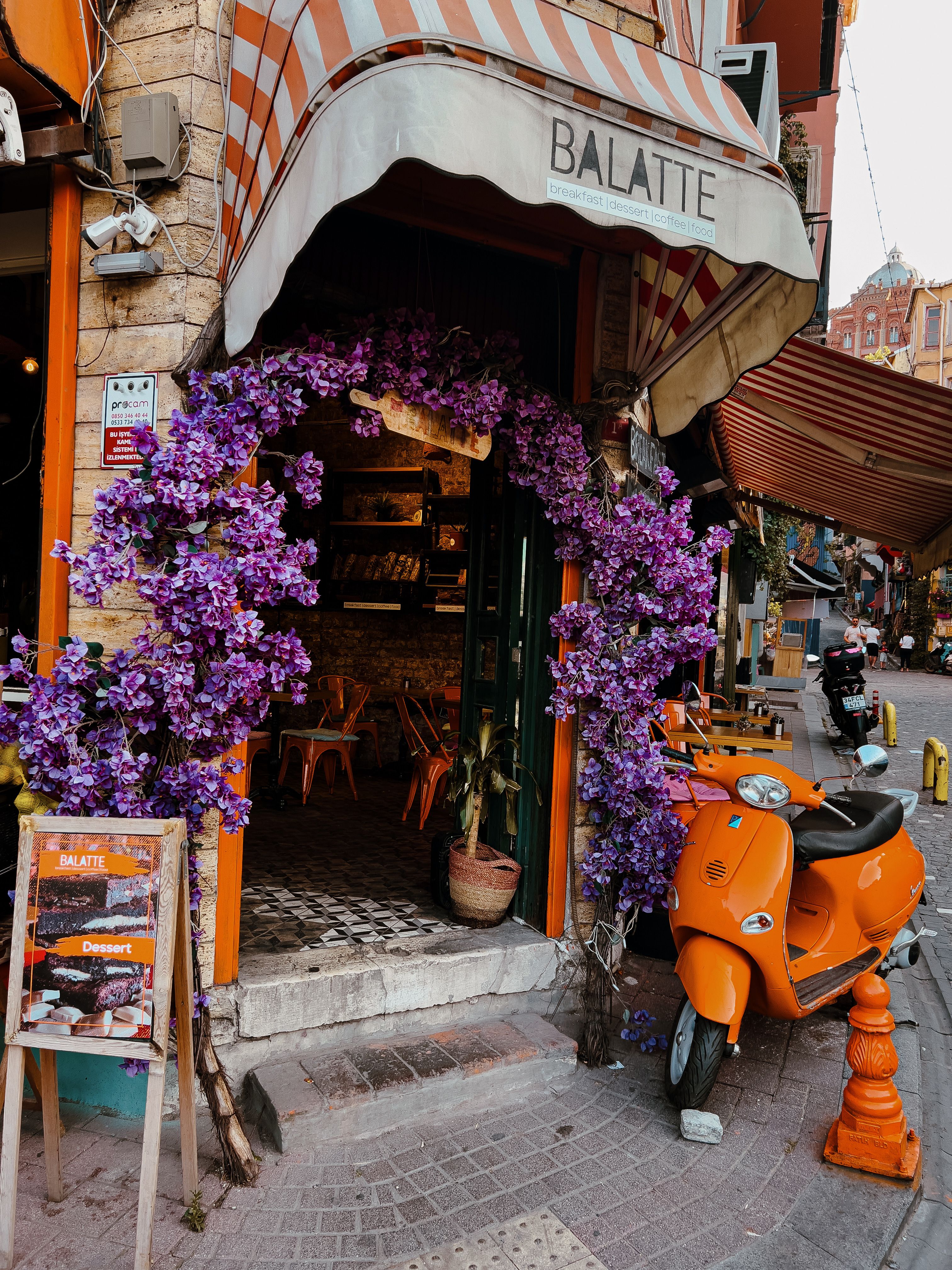 Colorful café entrance in Istanbul adorned with purple flowers and orange scooter.
