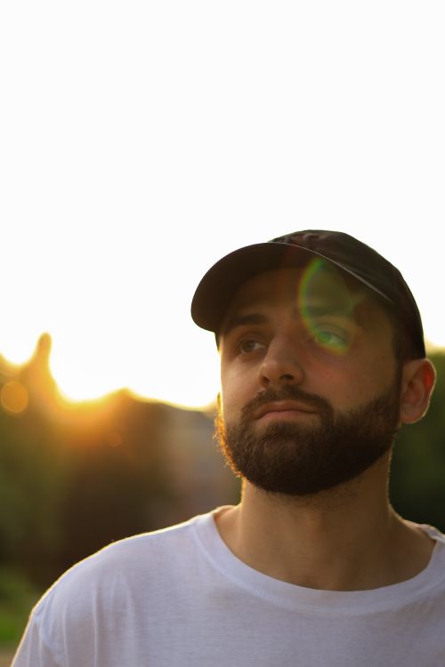 Free Portrait of a bearded man in a cap enjoying a summer sunset outdoors. Stock Photo