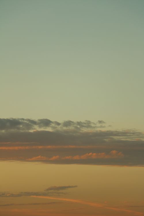 Free Serene view of a sunset sky with layered clouds and soft hues of orange and yellow. Stock Photo