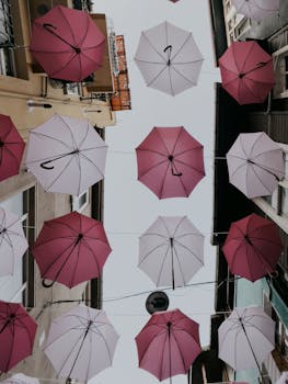 Artistic display of pink umbrellas hanging above a city alleyway, creating vibrant urban decor.