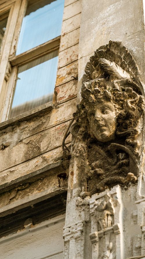 Free A detailed stone sculpture of a face on an old urban building facade, showing weathered textures. Stock Photo