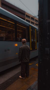 Moody street scene in Manchester with a tram passing by a lone pedestrian.