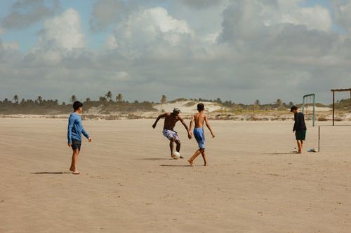 Free Group of young men playing soccer on a sandy beach under a sunny sky. Stock Photo
