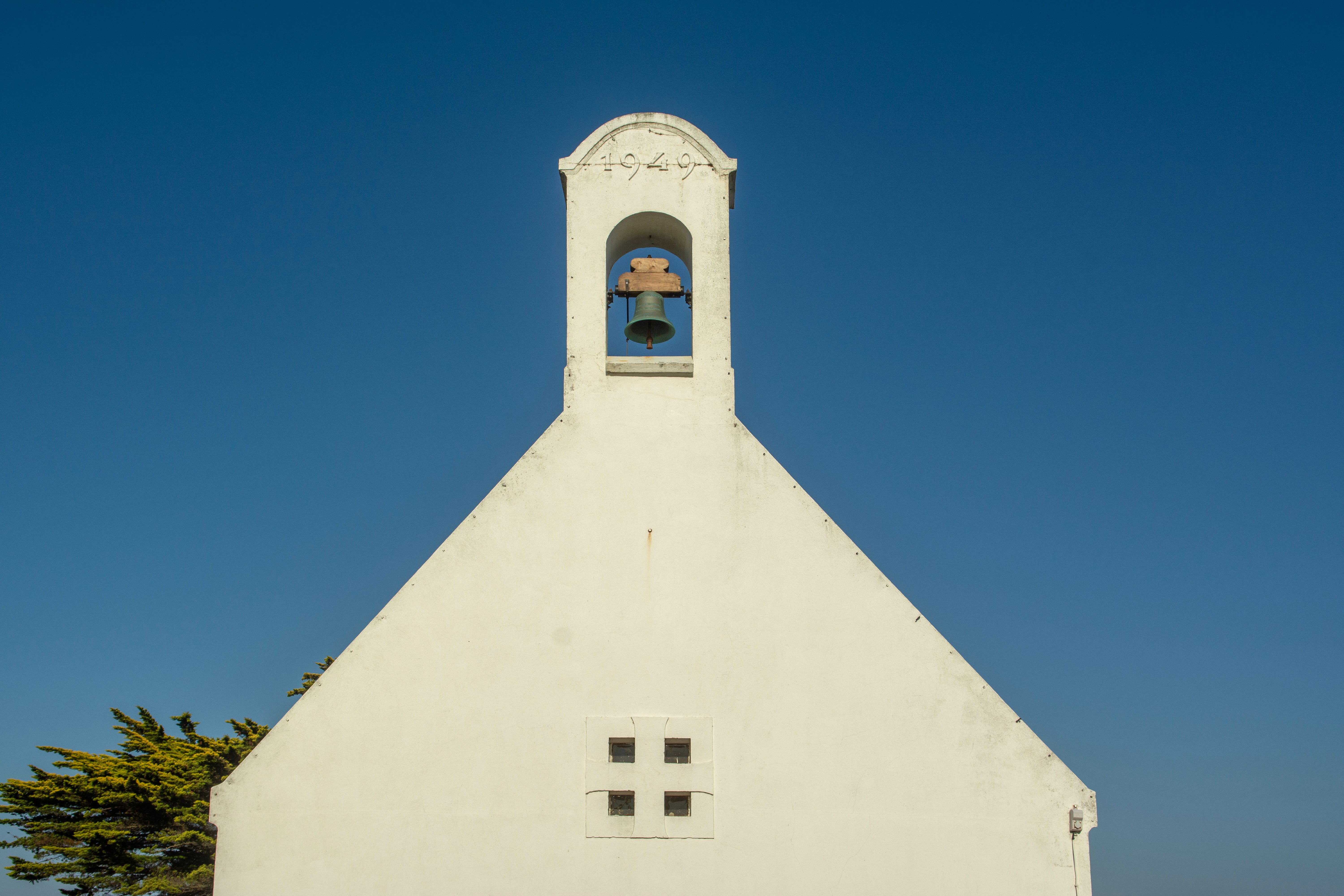 Minimalist photo of a white bell tower with clear blue sky, capturing simplicity and tranquility.