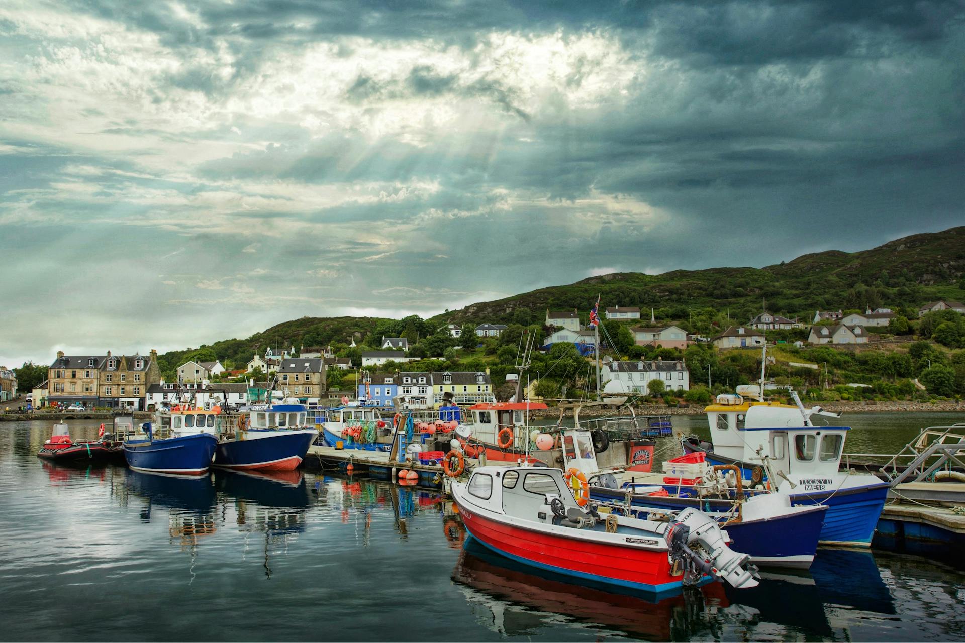 Picturesque fishing boats docked in Tarbert harbor, Scotland, under dramatic skies.