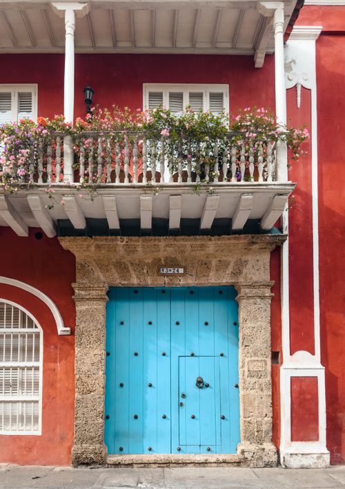 Free Charming colonial facade with vibrant red walls and a bright blue door, adorned by a flower-topped balcony. Stock Photo