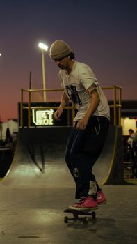 A stylish skateboarder performs tricks on a ramp at twilight in an urban skate park.