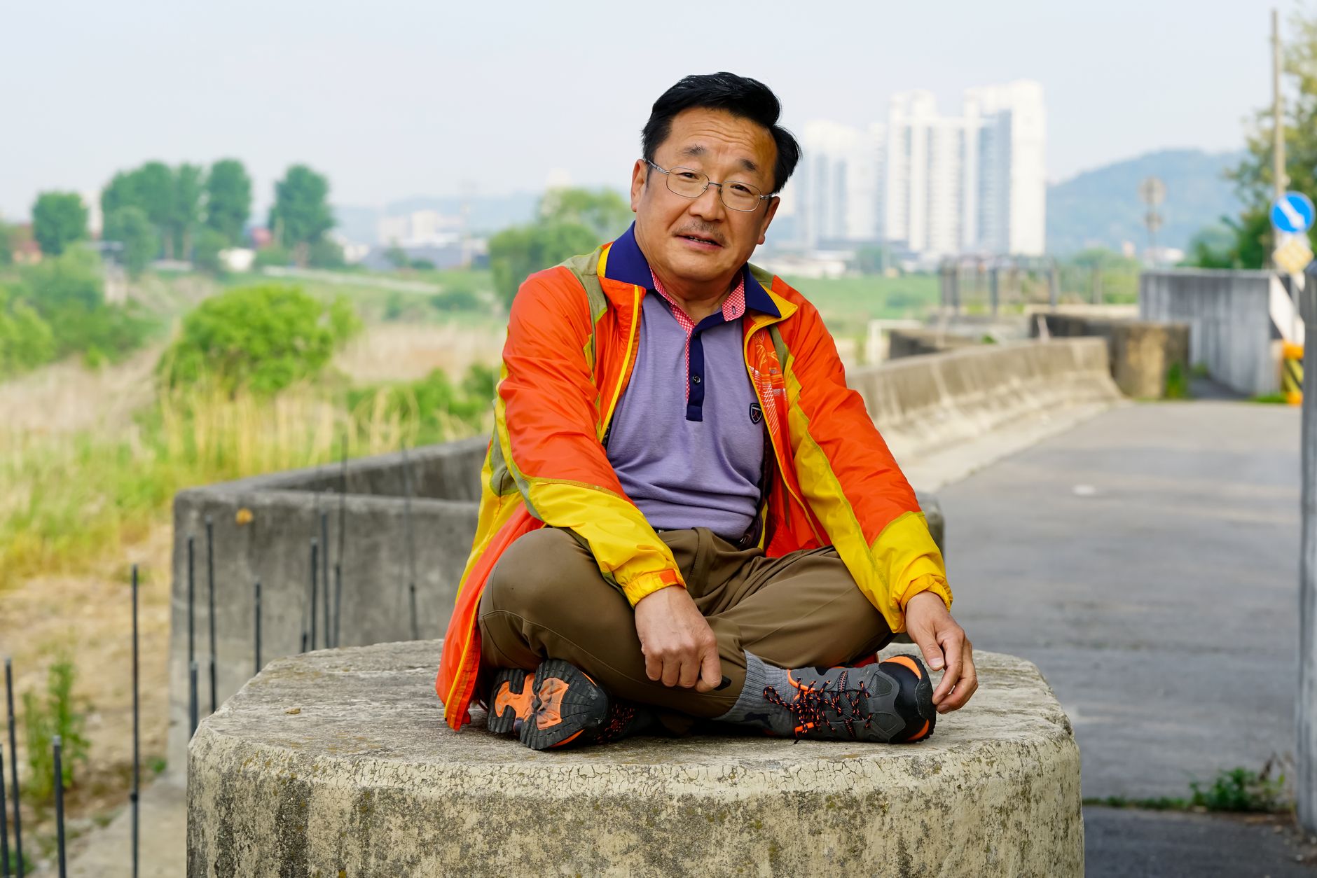 Elderly man sitting outdoors in urban area, dressed in colorful jacket, enjoying leisure time.