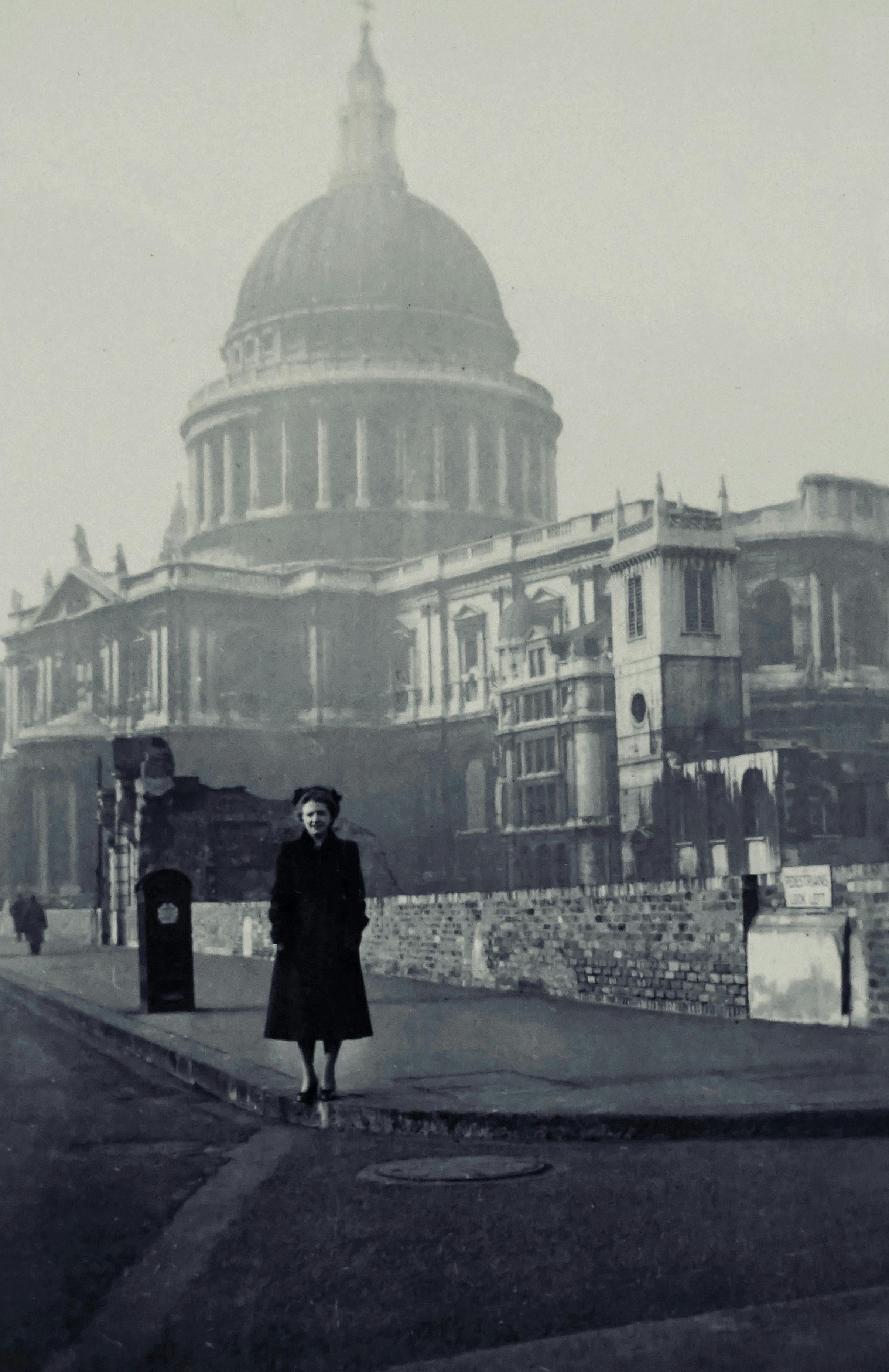 A black and white vintage photo of St Paul's Cathedral in foggy London with a woman standing in the foreground.