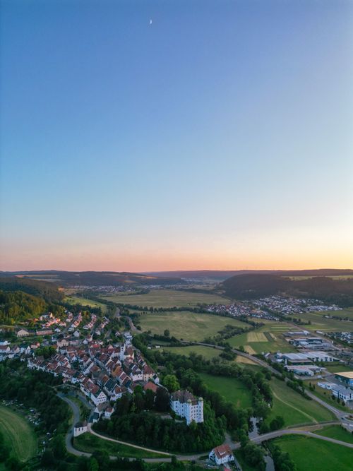 Free A breathtaking drone shot capturing a serene rural town during sunset with lush greenery and a clear sky. Stock Photo