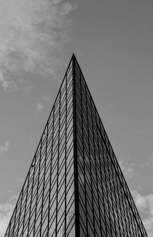Free Dramatic view of a modern triangular skyscraper against a cloudy sky, captured in black and white. Stock Photo