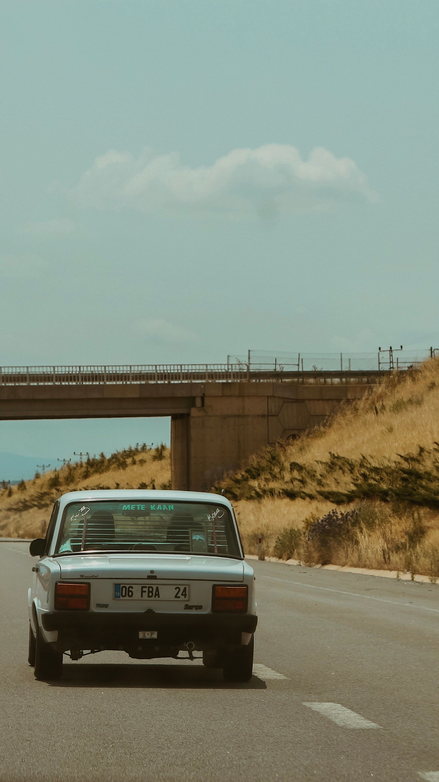 A classic car driving on a quiet highway under a blue sky.