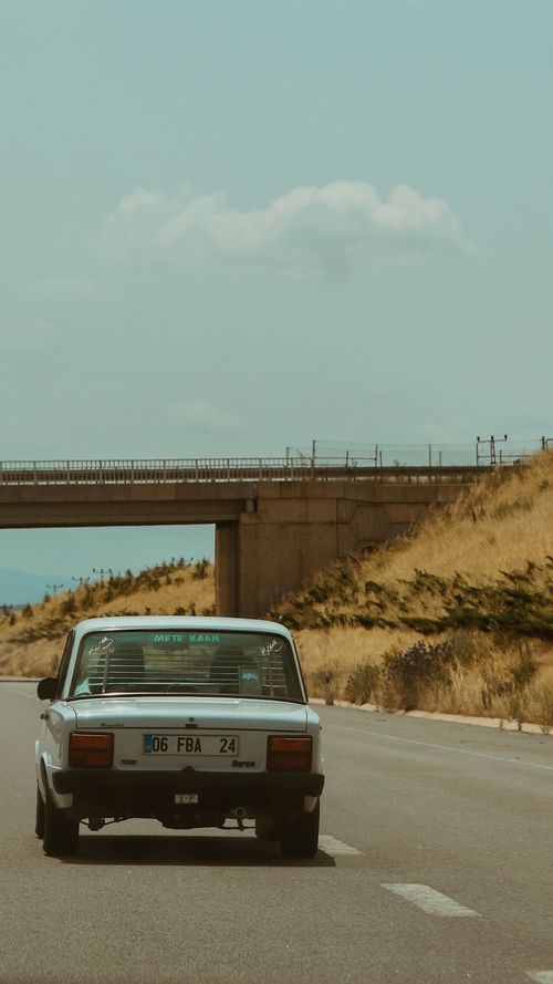 Free A classic car driving on a quiet highway under a blue sky. Stock Photo