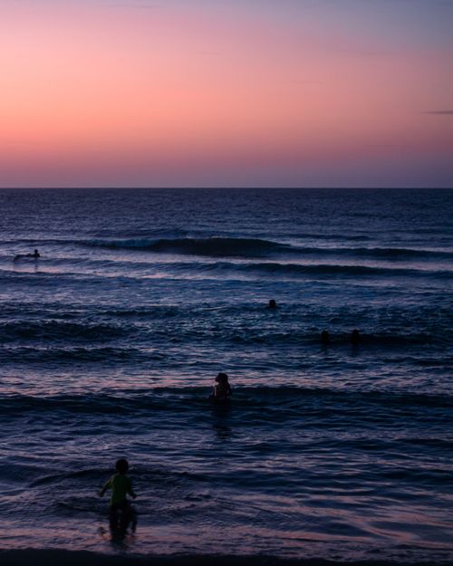 Free A scenic view of a Brazilian beach at dusk with silhouettes of swimmers enjoying the waves. Stock Photo
