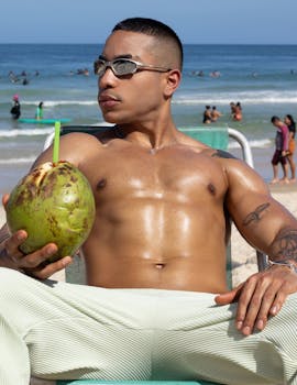 A man enjoys the Brazilian beach sun, holding a fresh coconut, with ocean waves in the background.