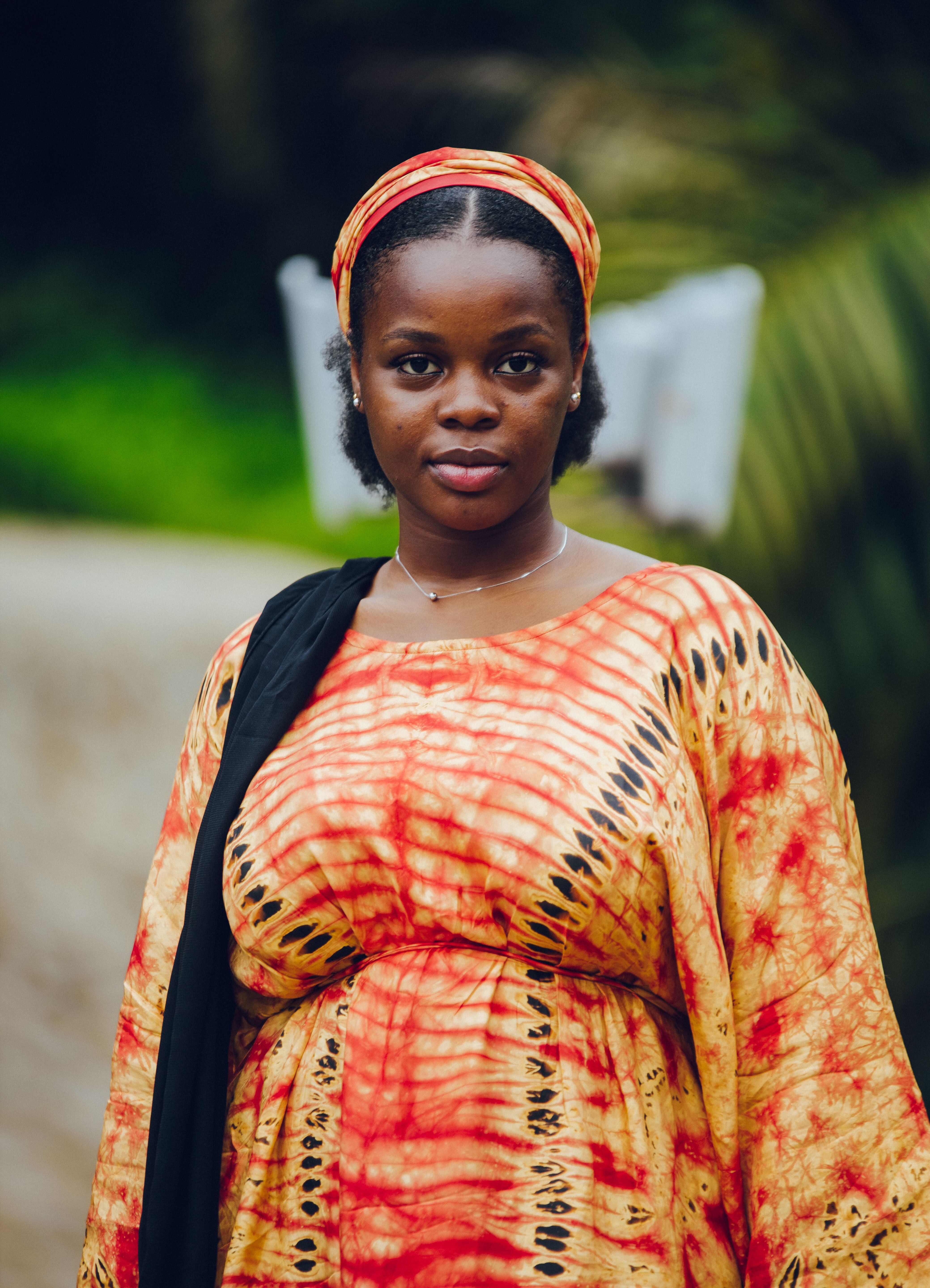 Portrait of a woman in traditional Nigerian attire with a vibrant dress and headwrap outdoors.