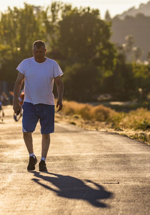 Free Adult man walking on a sunlit road in casual attire during sunset, casting a shadow. Stock Photo
