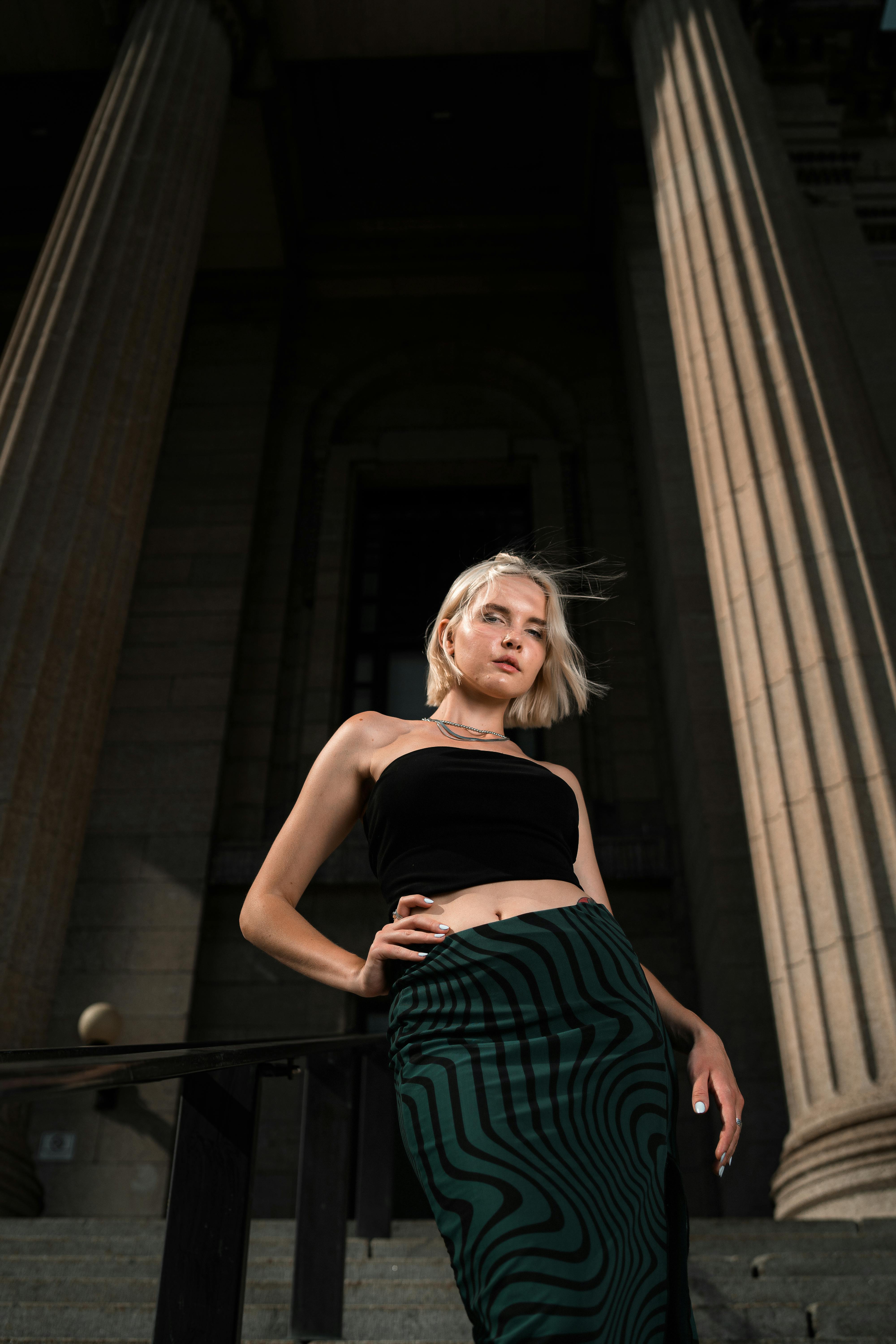 A woman in a black top and green skirt posing in front of a building