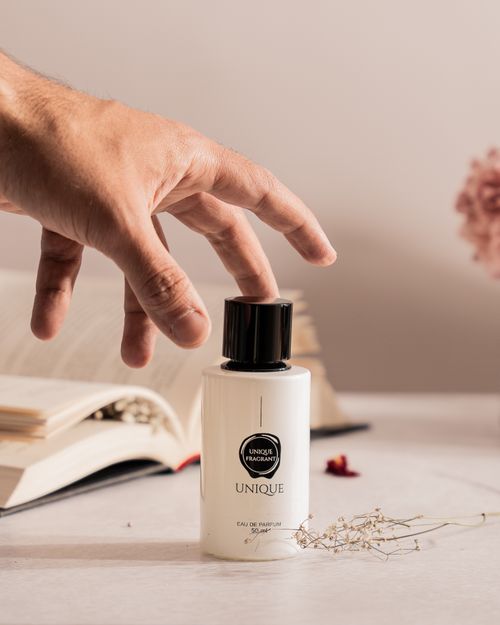 Free A hand reaches for a perfume bottle, set against a cozy backdrop with an open book. Stock Photo
