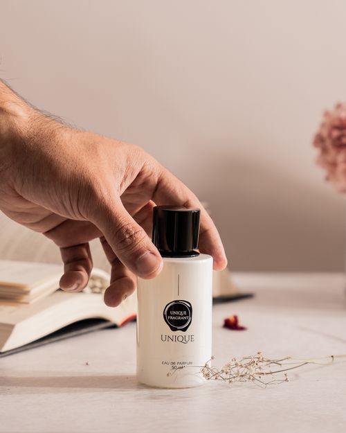 Free Hand reaching for a perfume bottle with books and flowers on a well-lit desk setting. Stock Photo