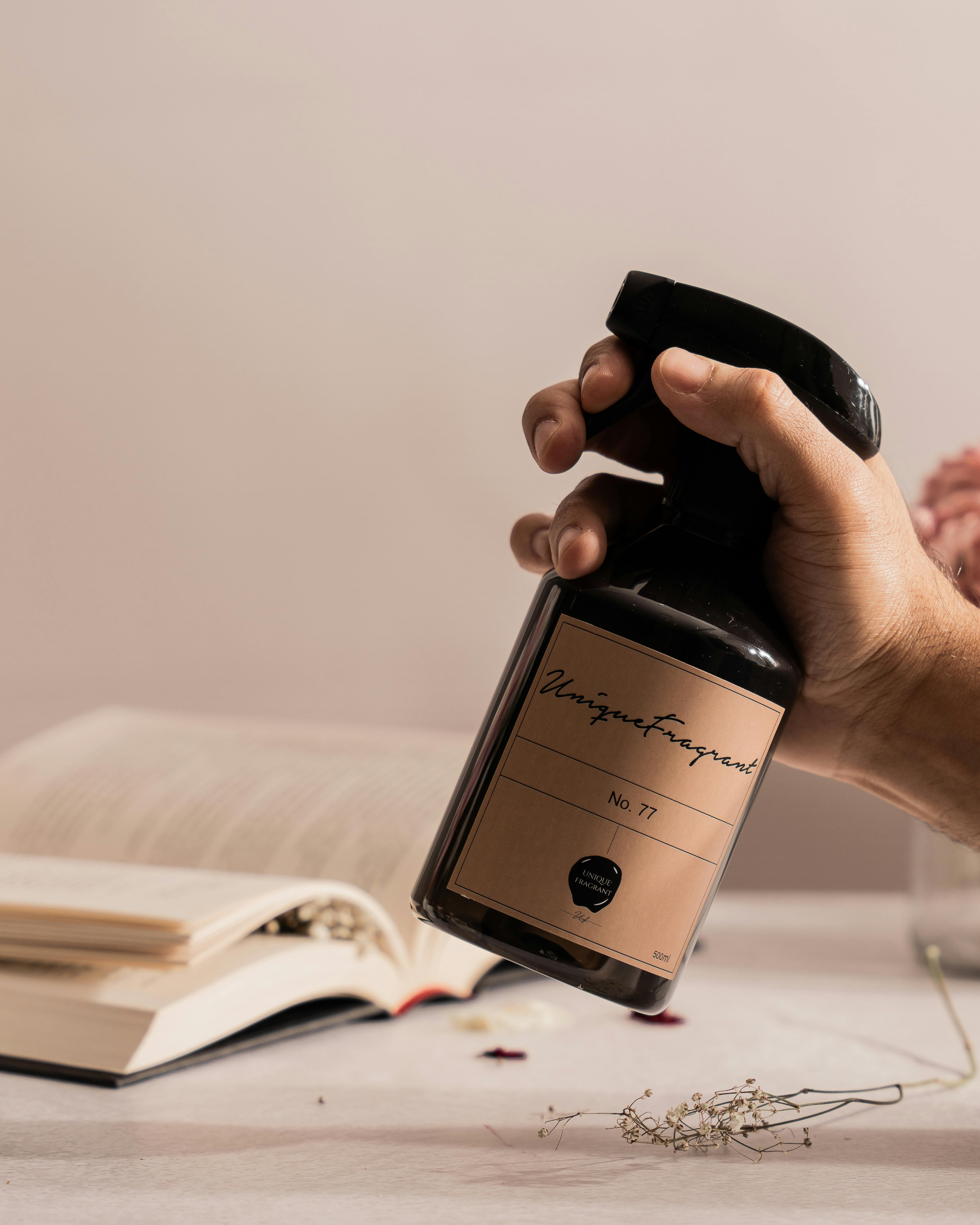 A hand holding a fragrance spray bottle beside an open book on a table.
