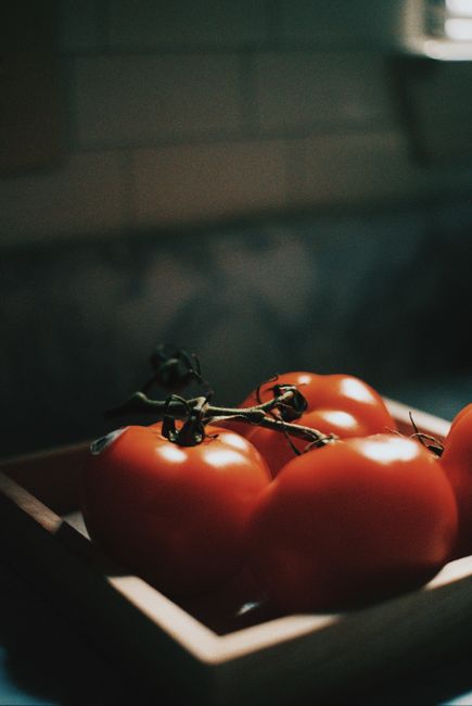 A close-up shot of fresh tomatoes in a wooden tray illuminated by soft natural light.