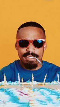 Portrait of a man wearing sunglasses with a birthday cake, featuring a vibrant yellow background.