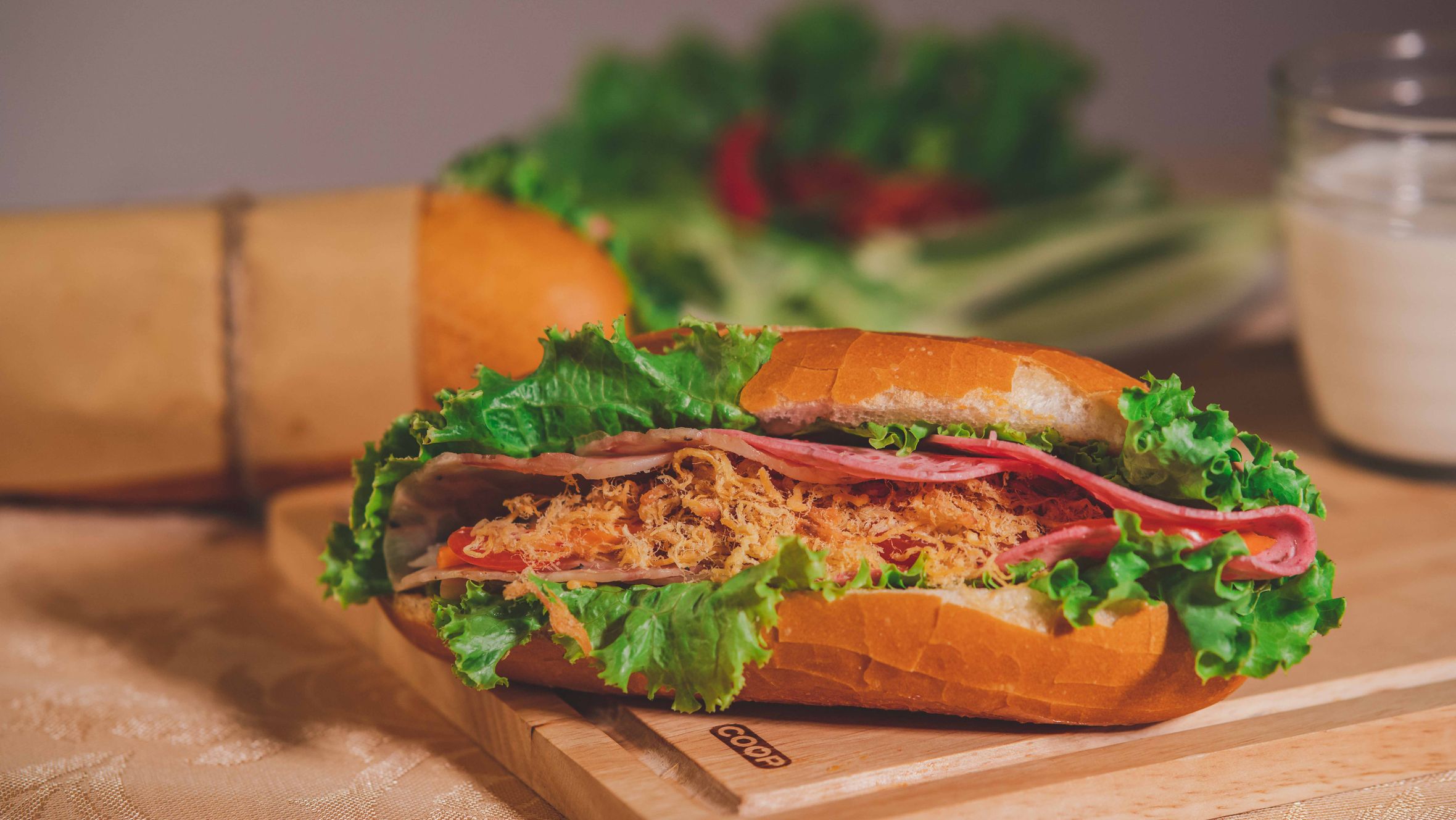 Close-up of a flavorful banh mi sandwich with fresh lettuce, meat, and bread on a cutting board.