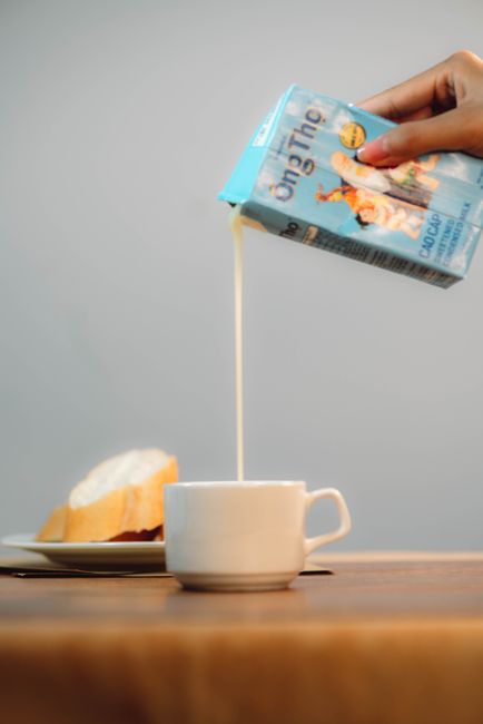 A glass measuring cup of milky-white half and half being poured, with a small pitcher of heavy cream and a carton of whole milk in the background.