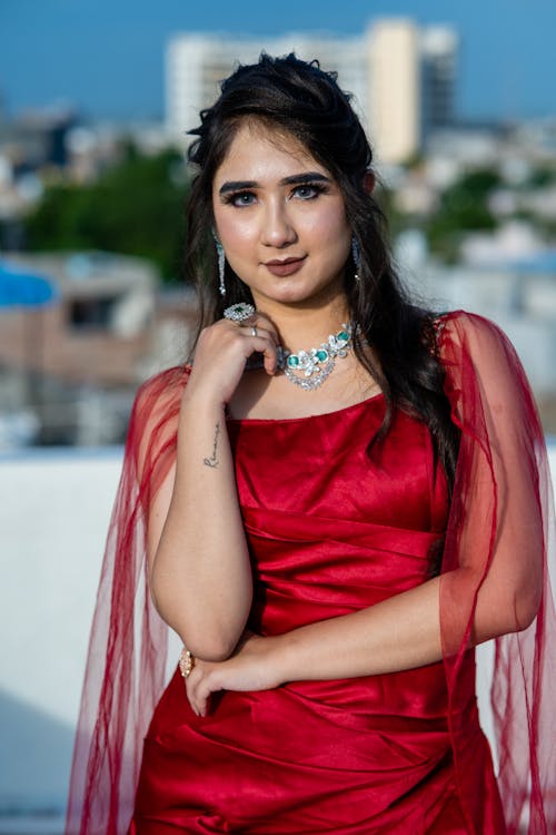 Young Woman in an Elegant Red Dress and Jewelry Standing Outside 