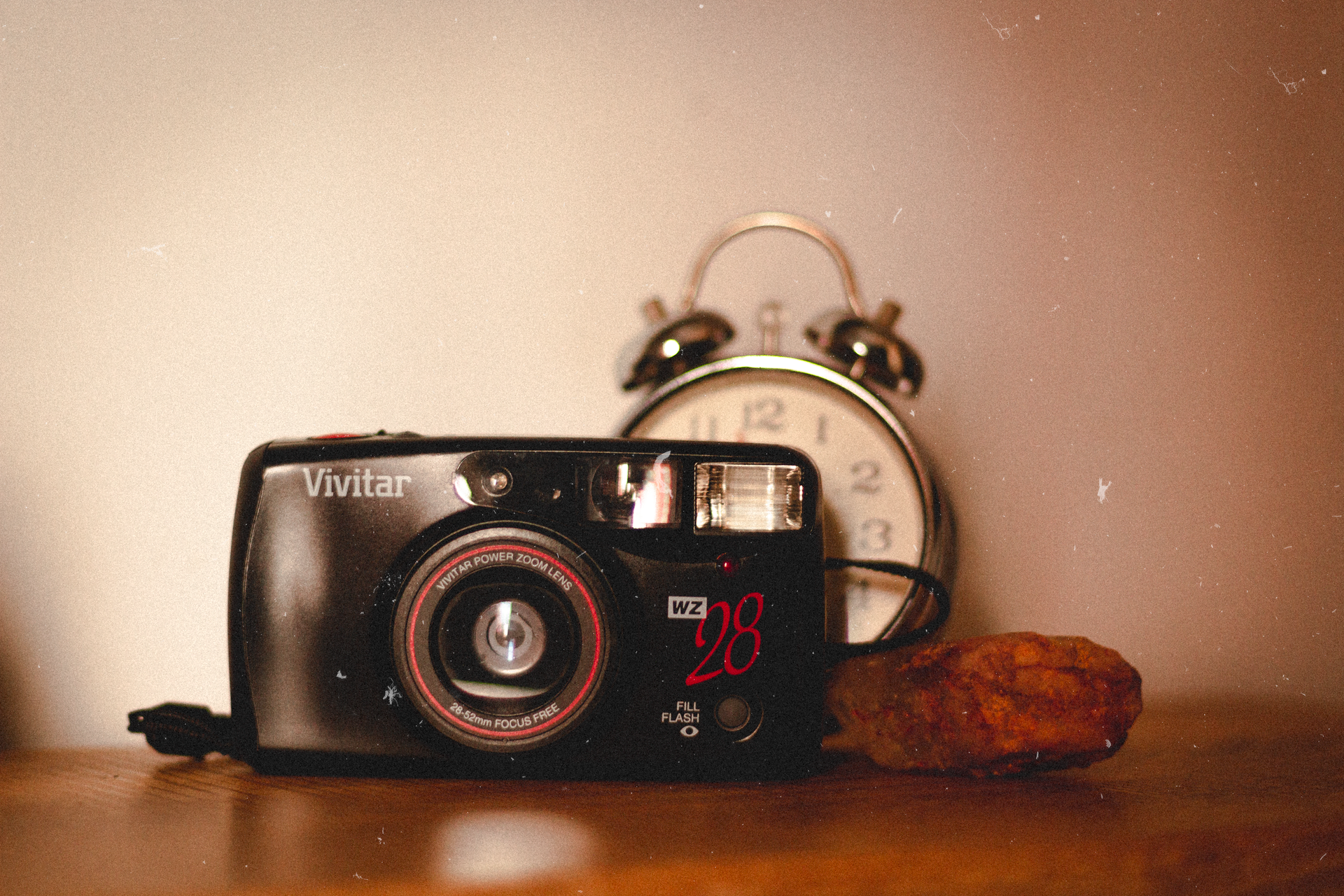 A retro camera with an alarm clock and a chicken nugget on a wooden surface.