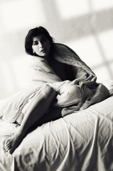 A woman wrapped in linens poses elegantly on a bed in a black and white artistic photo.