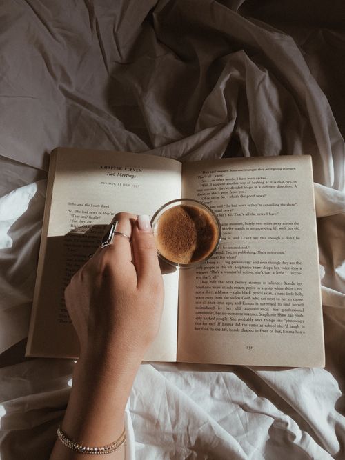 Free A person enjoys coffee and a book under soft sunlight, capturing a tranquil moment. Stock Photo