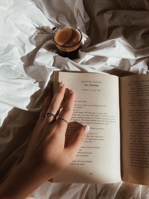 Cozy scene with a hand reading a book and coffee on bed.