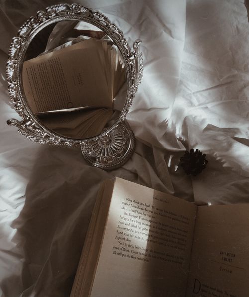 Free Intriguing still life featuring an open book and ornate mirror reflecting pages, captured in soft lighting. Stock Photo
