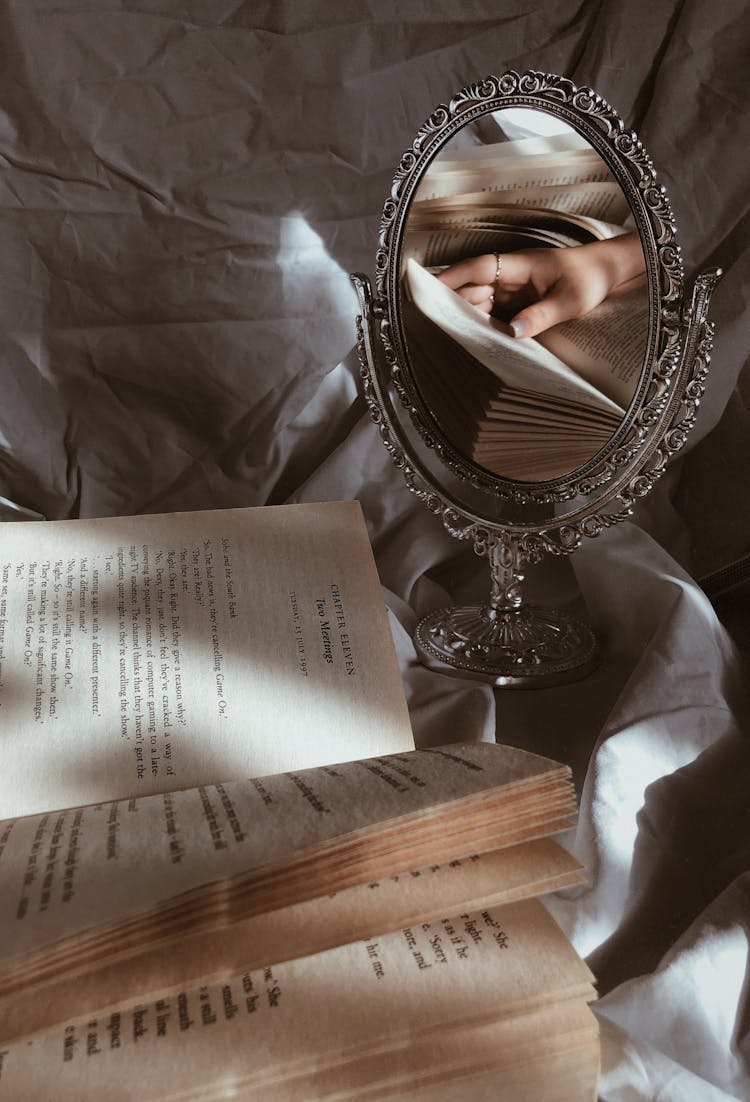 Book And Mirror With Reflection Of Woman Hand