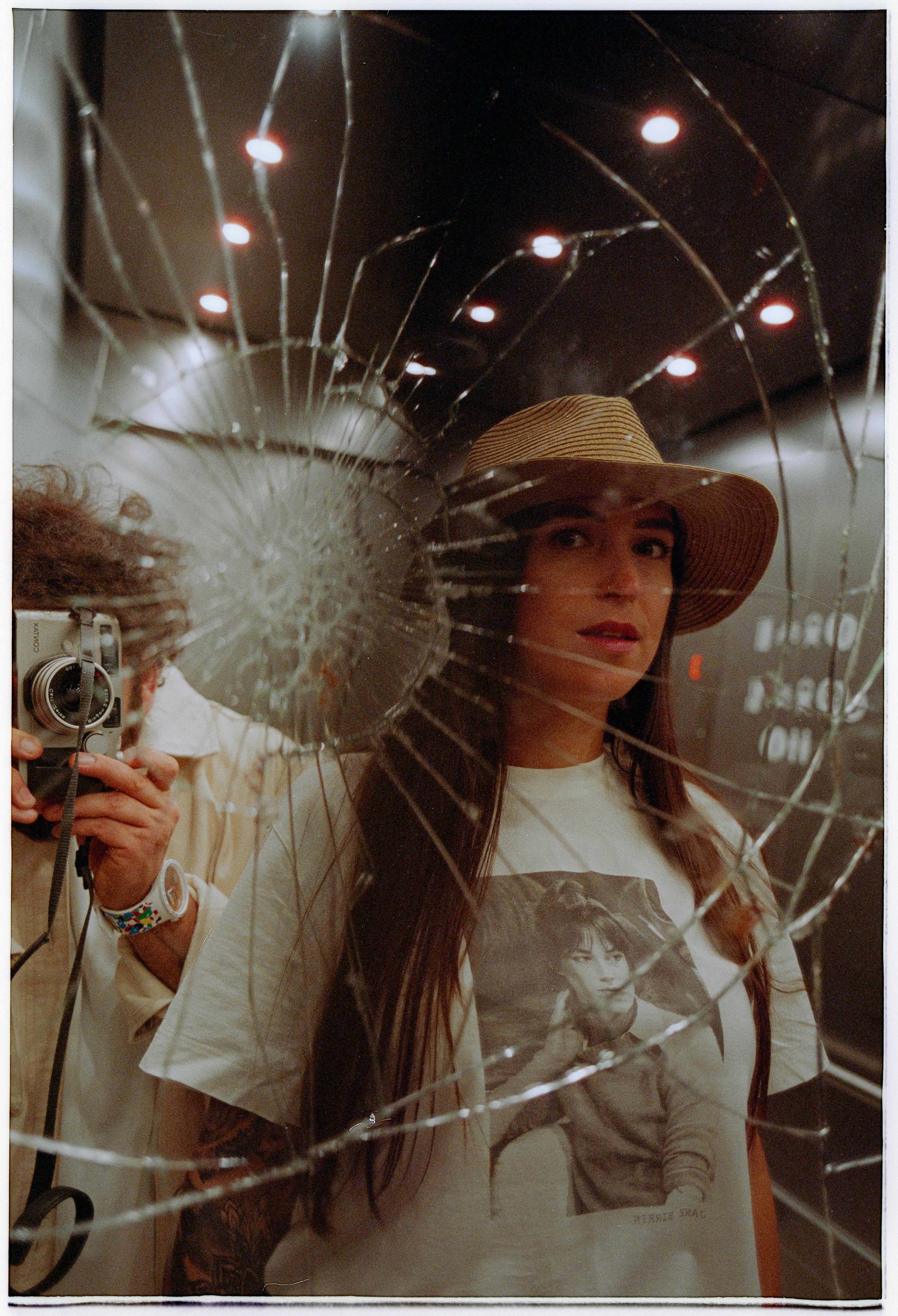 A woman and man creatively photographed through a cracked elevator mirror, utilizing reflection and contrast.