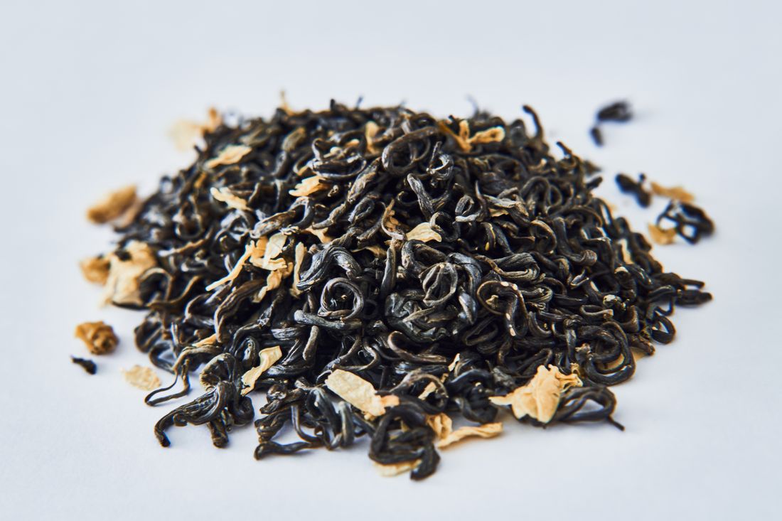 Pile of curled loose leaf tea with pale dried flower petals