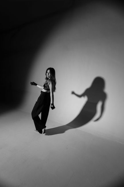 Elegant woman posing in a minimalist studio, casting a dynamic shadow, in black and white.